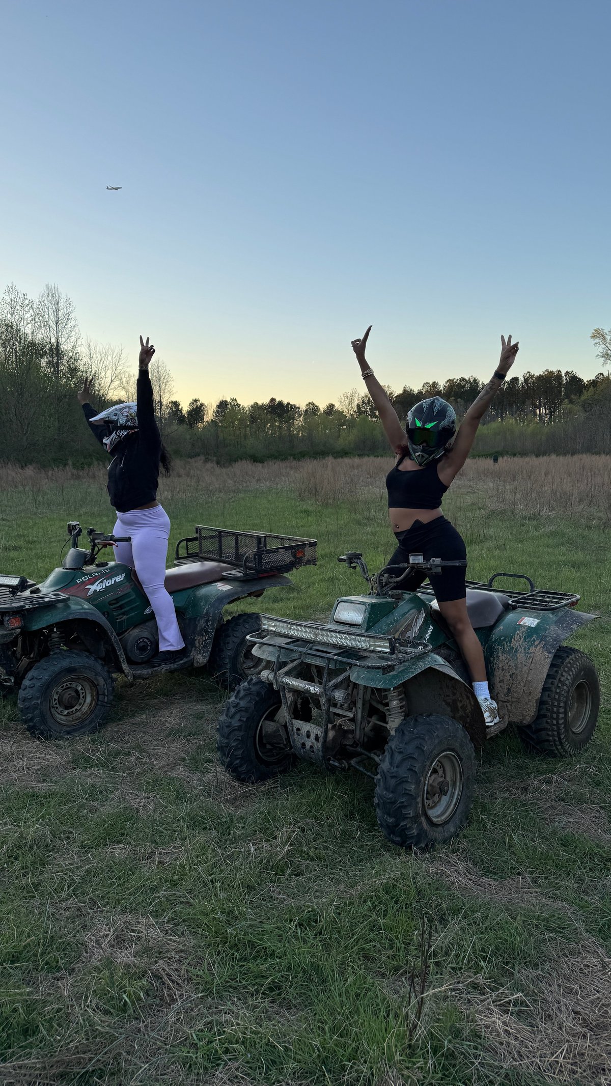 Two women on ATVs celebrating with arms raised in an open field at sunset